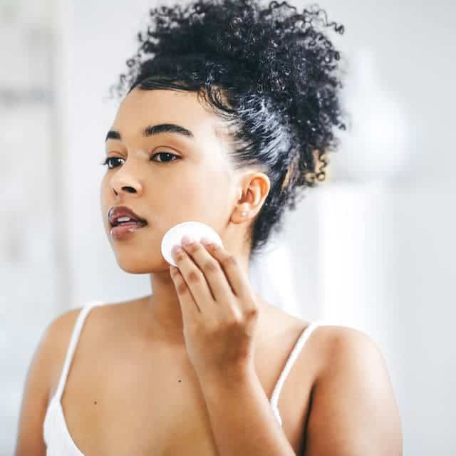 A view of a girl with curly hair removing her makeup off with a wipe