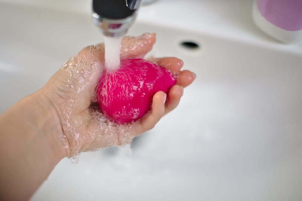 girl cleans in her hand a pink rosa beauty blender for make up with water