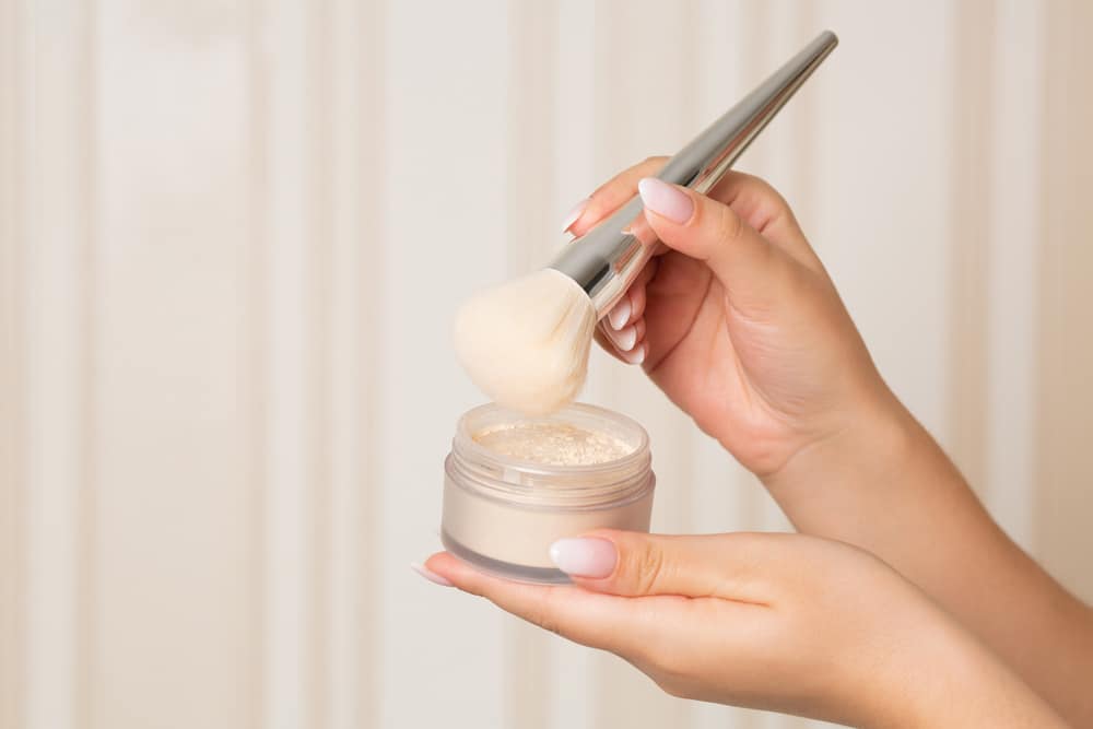 Woman With A Brush Using Loose Powder On A Beige Background 