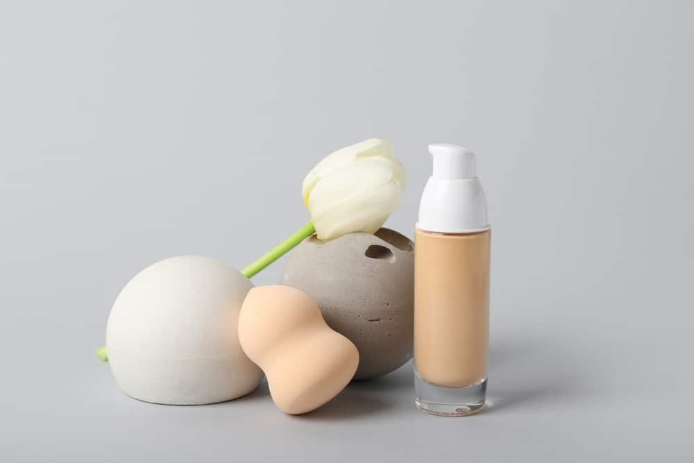 bottle of makeup foundation and tulip flower on grey background