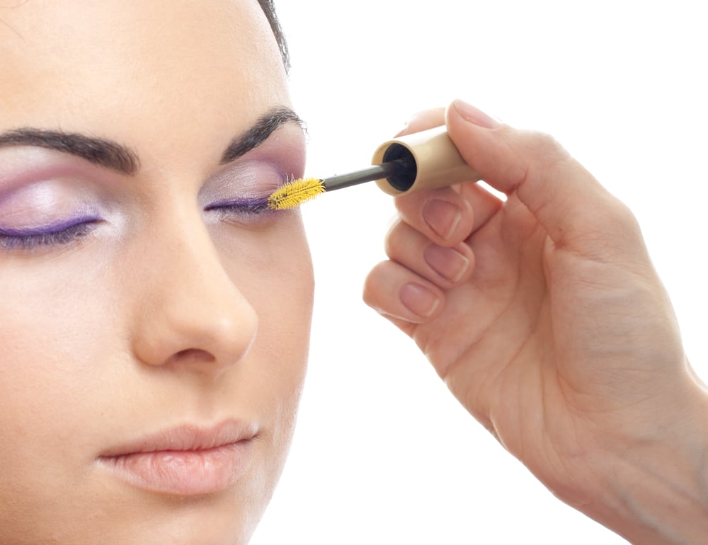 A view of a hand applying mascara on purple glossy eyelids